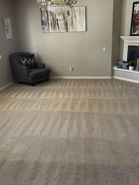 Clean, freshly vacuumed carpet in a living room setting, featuring a gray chair with a patterned cushion, wall art, and a fireplace, showcasing the effectiveness of professional carpet cleaning services in Bakersfield.